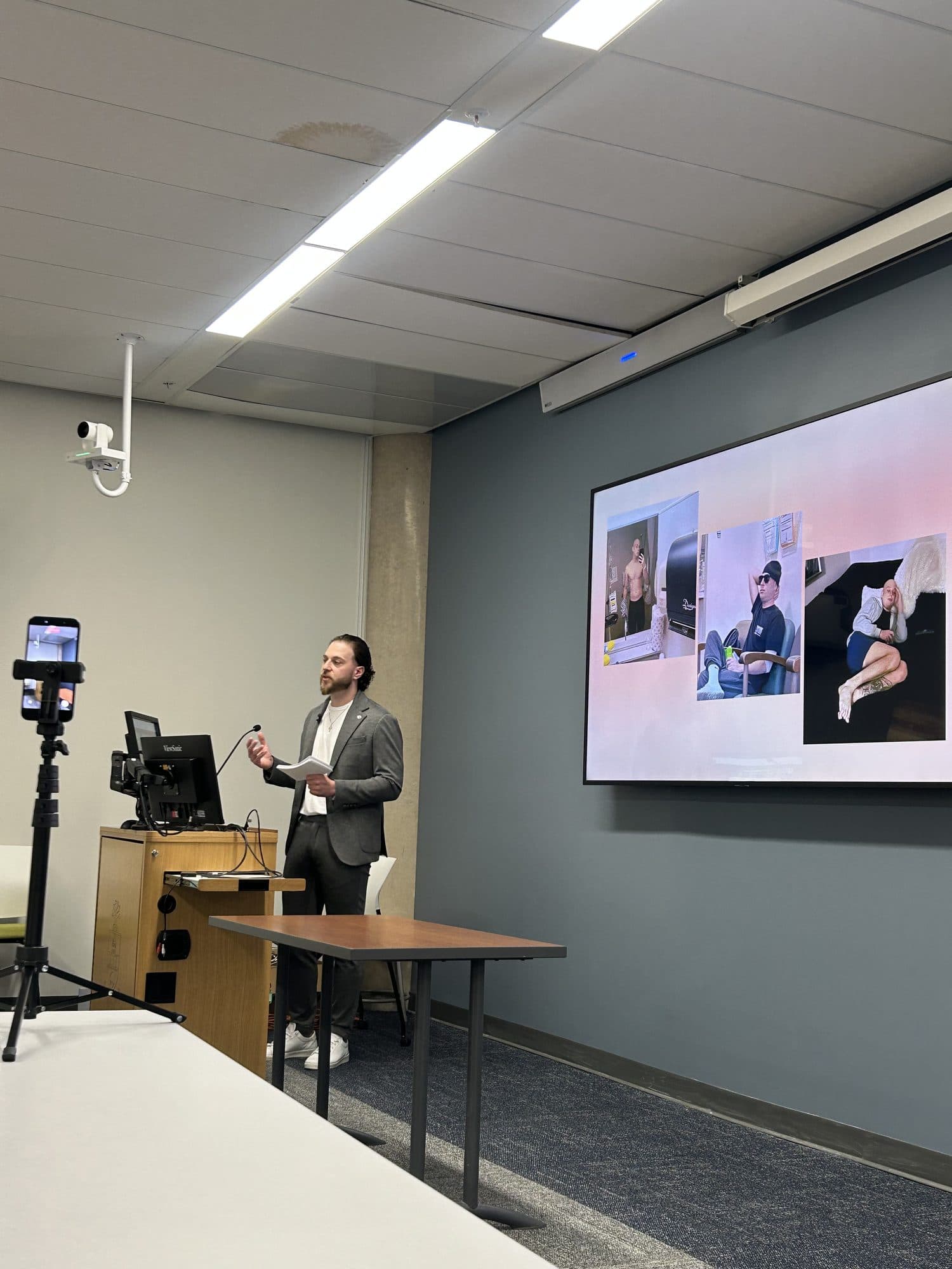 Michael speaking at a lectern in front of a screen showing photographs from his cancer treatment